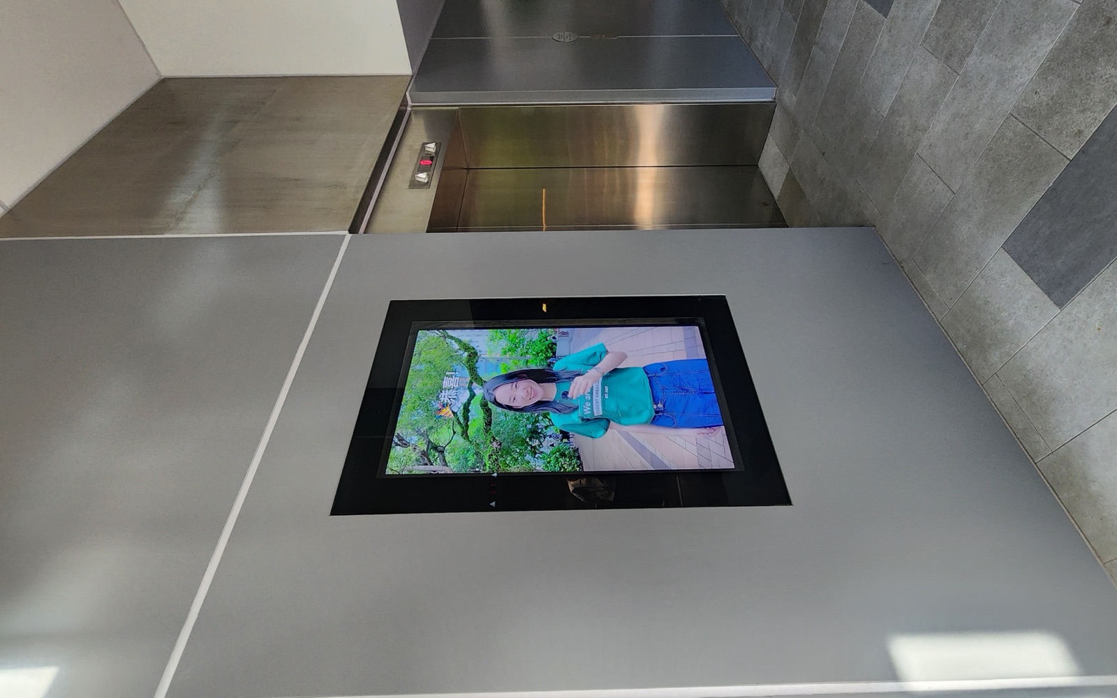 A U-Vision portrait screen set into the wall above the lift lobby in East Gate
