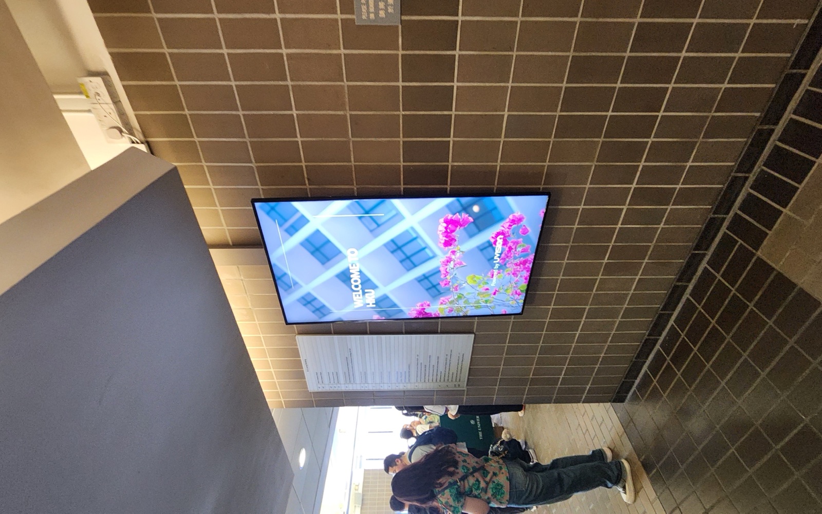 A U-Vision portrait screen mounted on the tiled wall of the covered walkway beside K.K. Leung Building