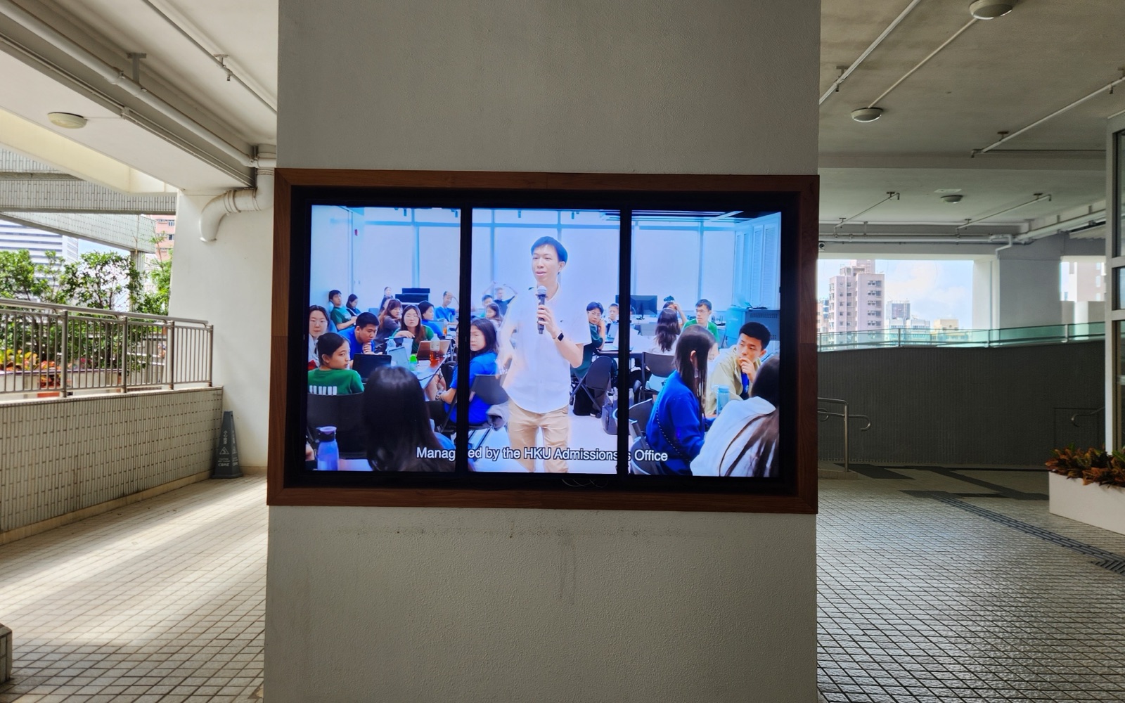 A U-Vision screen set into the timber-framed display case beside the glass entrance of Knowles Building