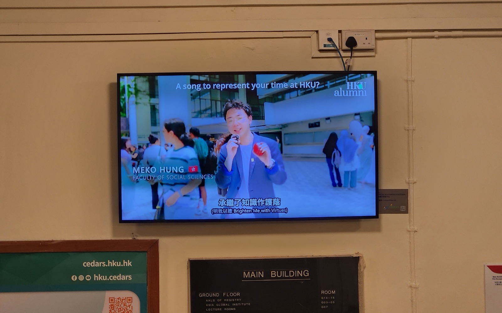 A U-Vision screen mounted on the ground-floor corridor wall of the Main Building, beside the room directory