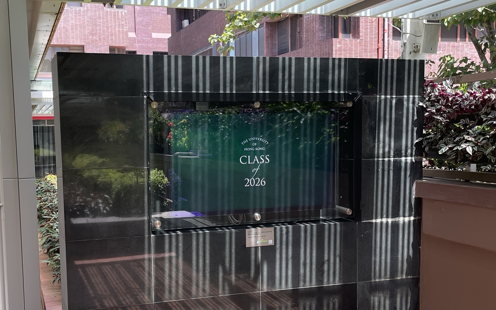 A U-Vision screen set into the polished stone wall of the covered walkway on University Street